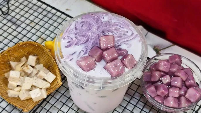 Bàn tay đang khuấy đều ly trà sữa khoai môn tươi, thể hiện quá trình pha chế tỉ mỉ để có thức uống thơm ngon.