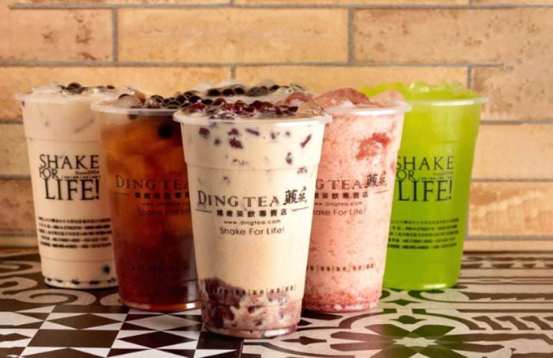 Một ly trà sữa Ding Tea với trân châu đen và một ống hút xanh, đặt trên nền đá cẩm thạch