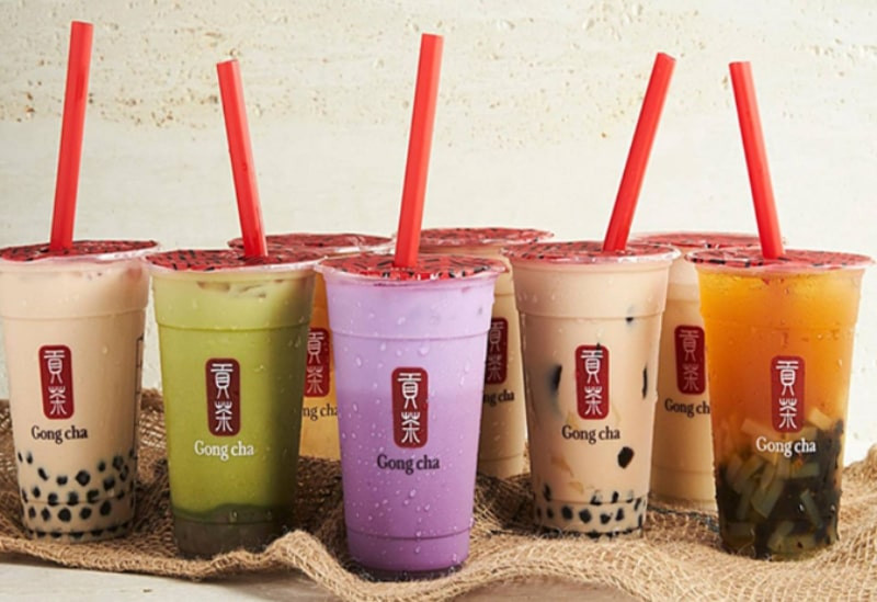 Một ly trà sữa Gongcha với kem sữa và trân châu, đặt trên nền trắng cùng hình ảnh các loại topping khác