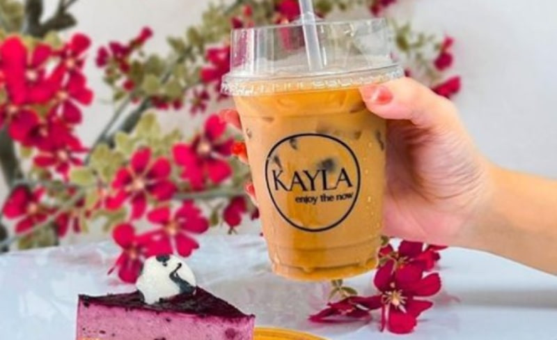 Một ly trà sữa Kayla Coffee với lớp kem sữa trắng và trân châu đen, được đặt trên một khay gỗ