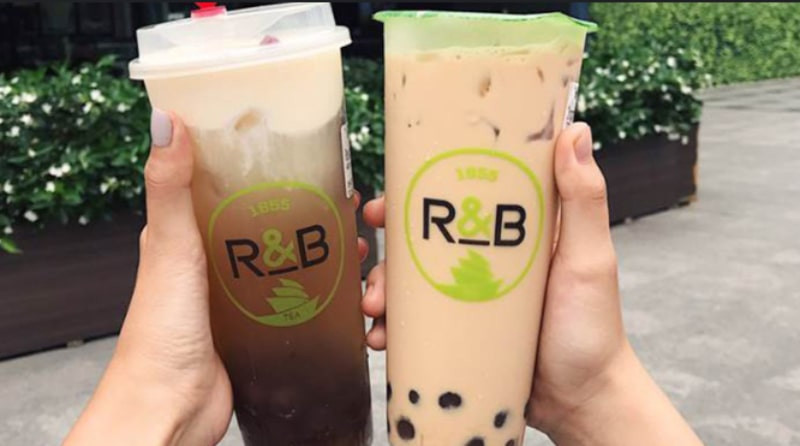 Một ly trà sữa R&amp;B Tea với kem cheese và trân châu, đặt trên bàn gỗ cùng ánh đèn vàng