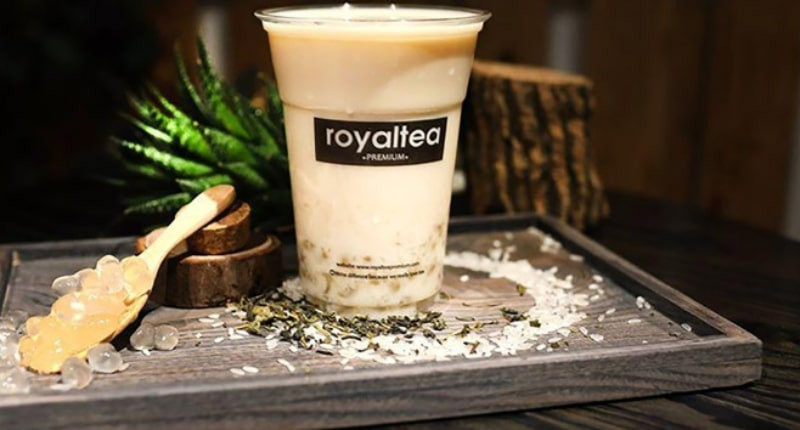 Một ly trà sữa Royaltea với lớp kem cheese dày và bột matcha rắc lên, đặt trên bàn gỗ
