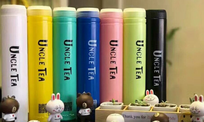 Một ly trà sữa Uncle Tea với lớp kem cheese và trân châu, đặt trên bàn đá cùng với hoa văn