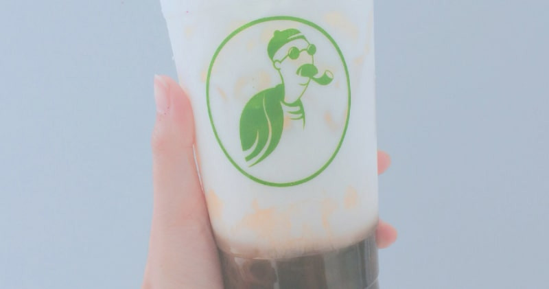 Một ly trà sữa Woozi với lớp kem sữa và topping đặc biệt, đặt trên nền tối