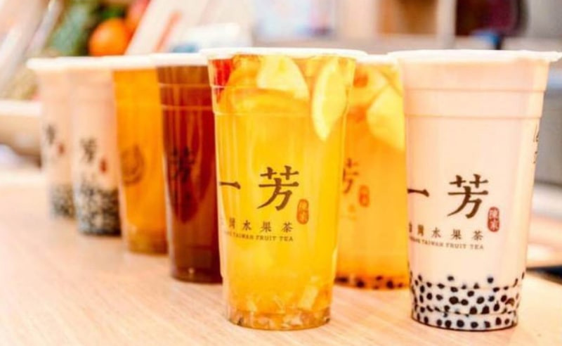 Một ly trà sữa Yi Fang với trái cây tươi cắt lát bên trong, đặt trên bàn gỗ