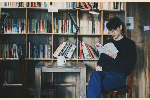 Một người cầm sách, tạo dáng bên ly trà sữa, chụp ảnh sống ảo tại quán cafe với phong cách tri thức.